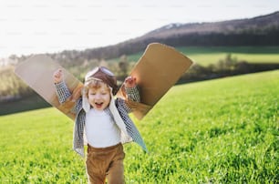 Happy toddler boy avec chapeau, lunettes et ailes jouant dehors dans la nature printanière. Concept pilote et vol.