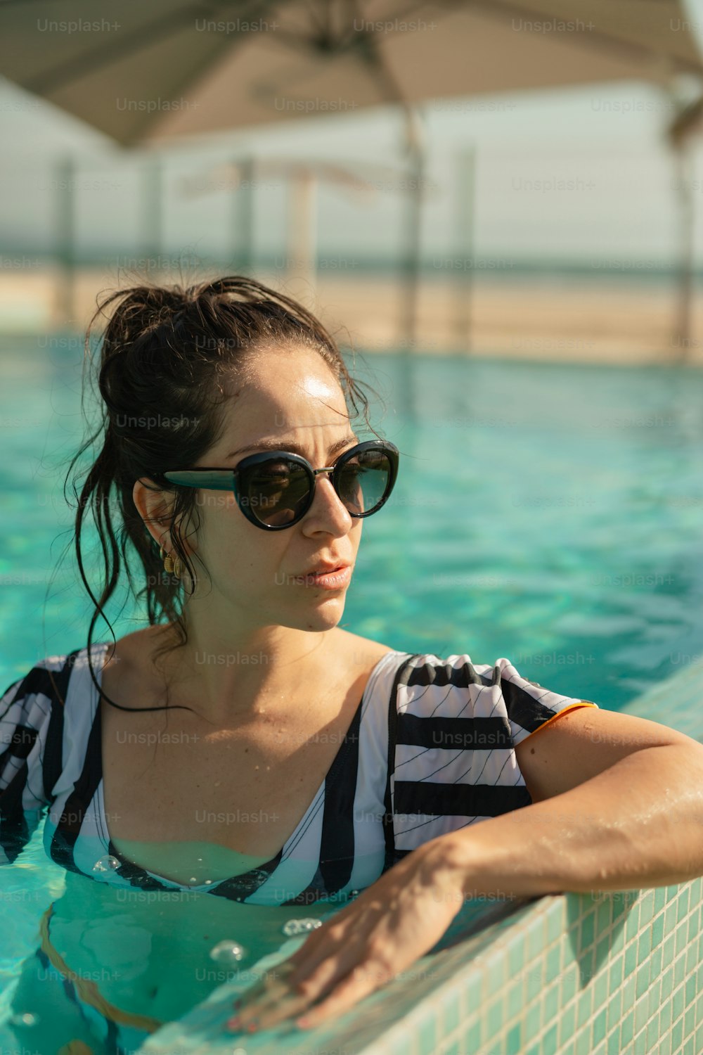 Una mujer en una piscina con gafas de sol y una camisa a rayas