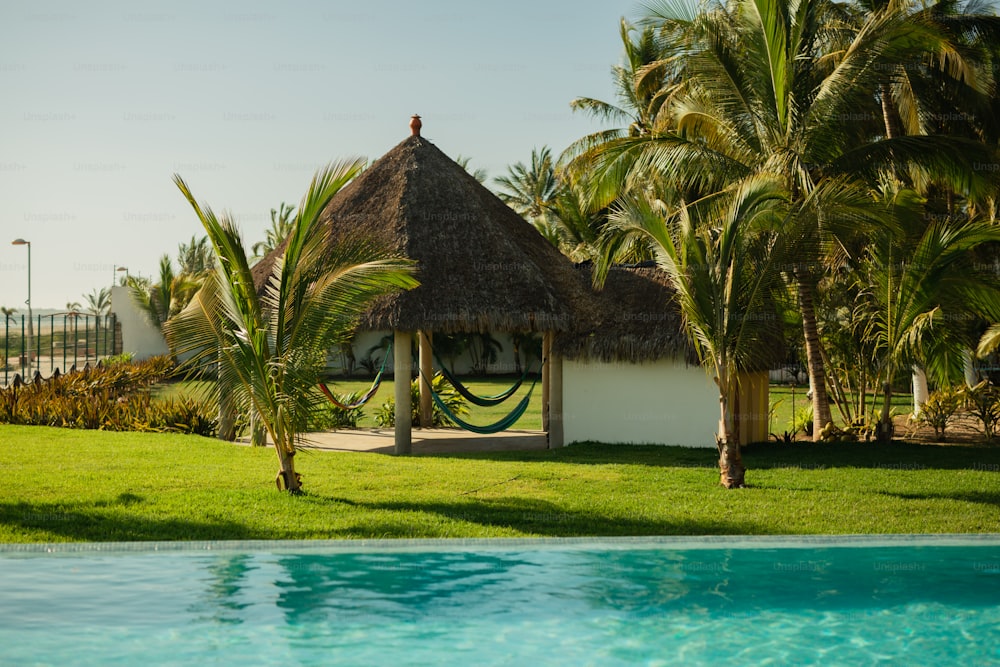 a small hut with a thatched roof next to a pool