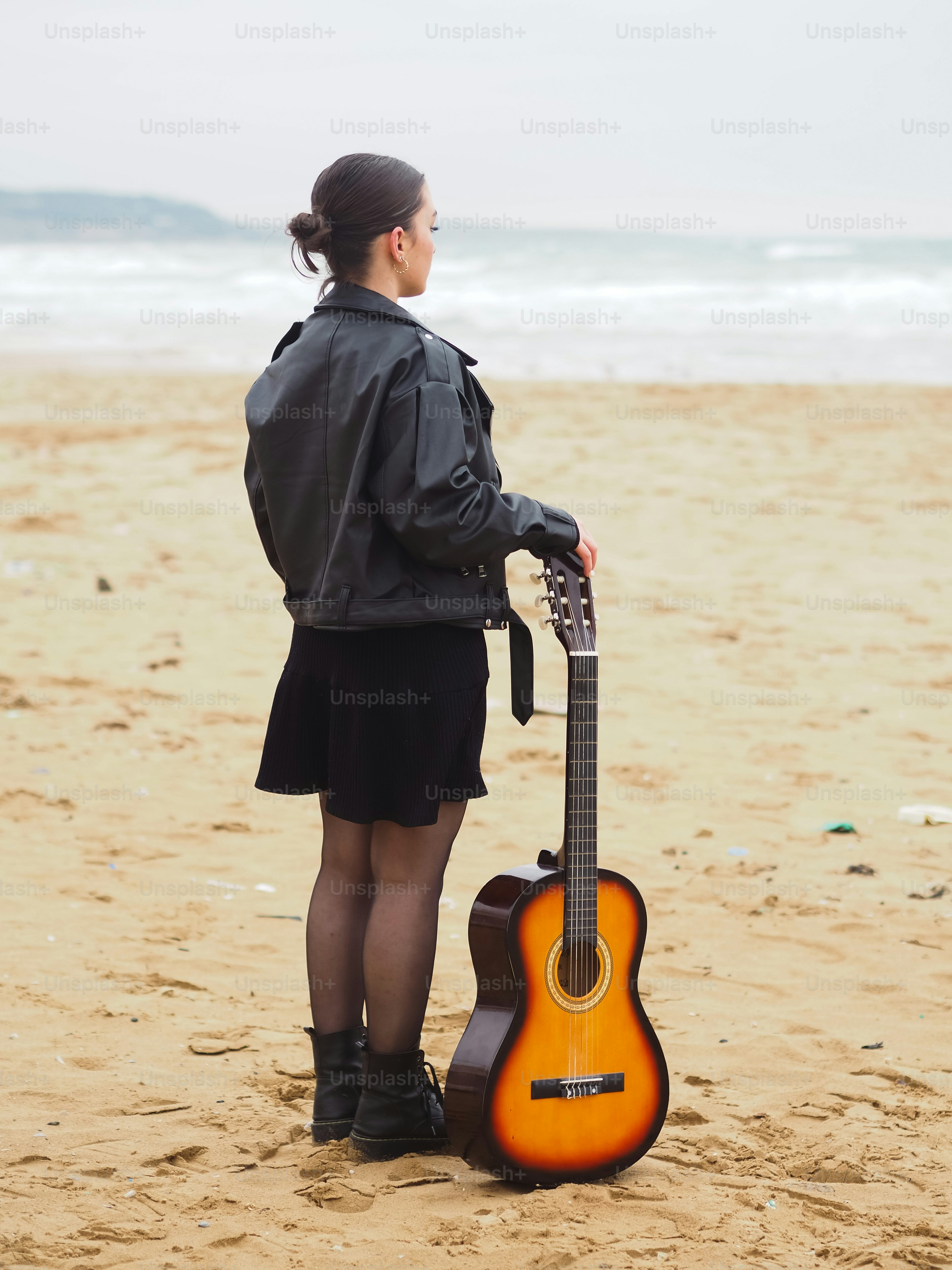 Una mujer parada en una playa sosteniendo una guitarra