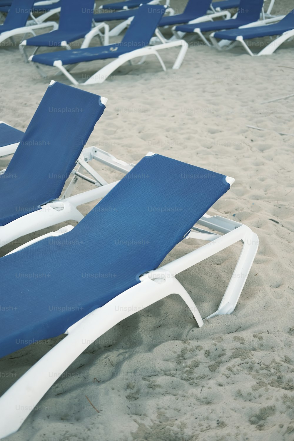 um par de cadeiras de gramado sentadas em cima de uma praia de areia