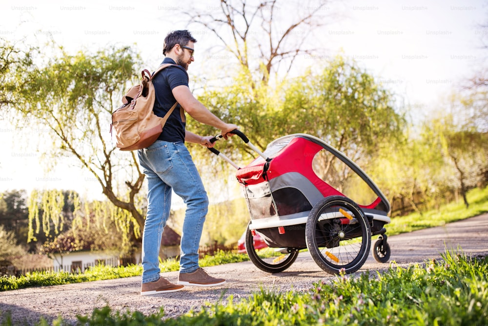 A father with backpack and jogging stroller on a walk outside in spring nature.