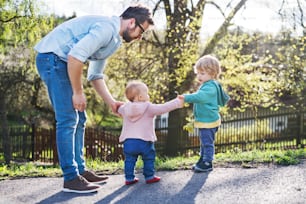 A father with his two toddler children outside on a sunny spring walk.