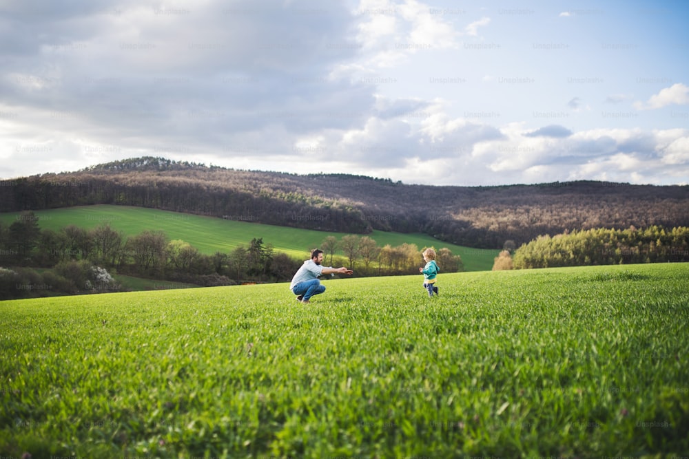 A mature father with his toddler son running outside in green sunny spring nature.