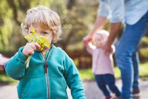 Un padre irriconoscibile con i suoi due bambini piccoli fuori in una soleggiata passeggiata primaverile.