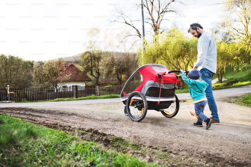 A father with toddler son pushing a jogging stroller outside. A walk in spring nature.