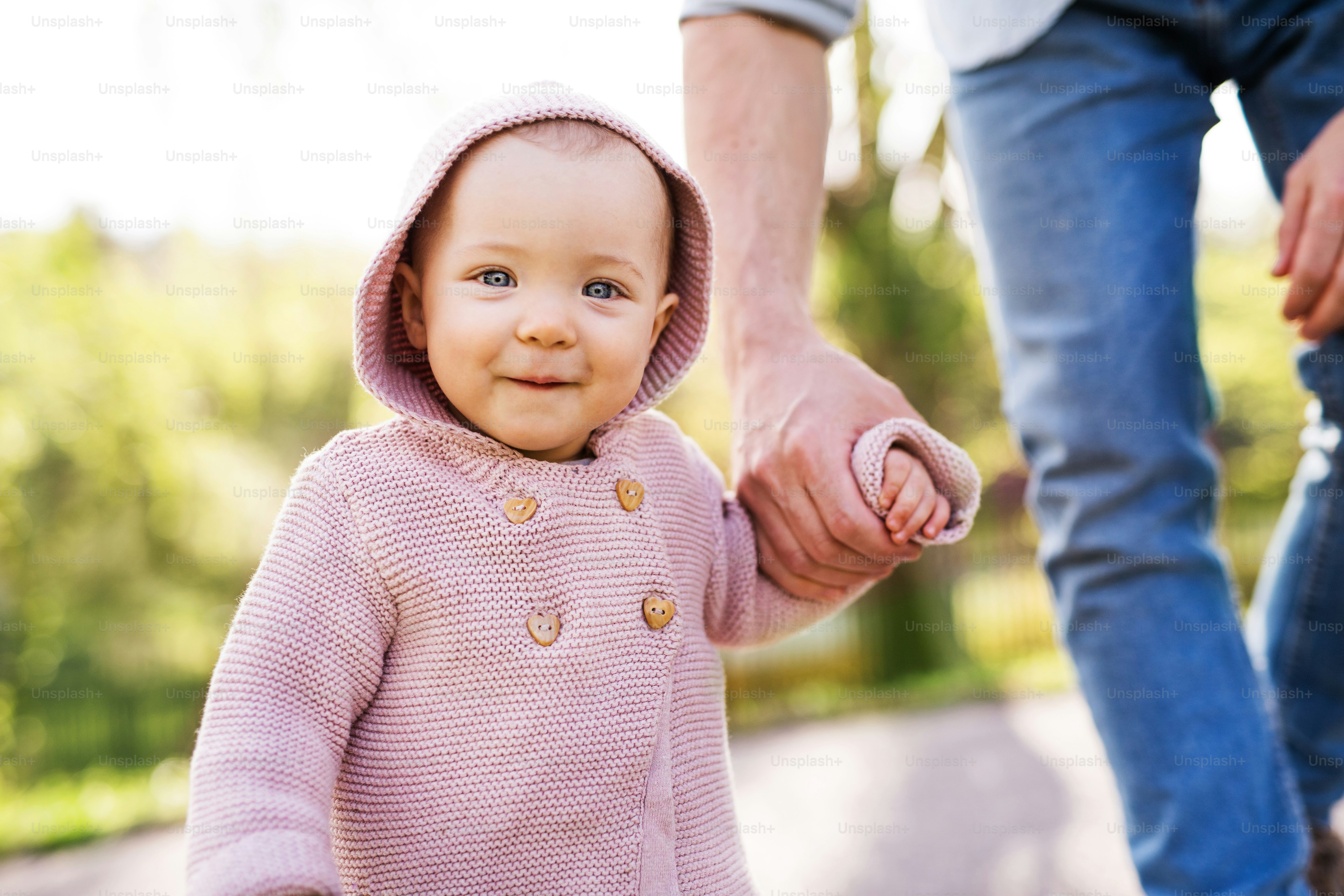 An unrecognizable father with his toddler daughter outside in green sunny spring nature.