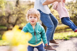 Un père méconnaissable avec ses enfants en bas âge dehors lors d’une promenade printanière ensoleillée, s’amusant.