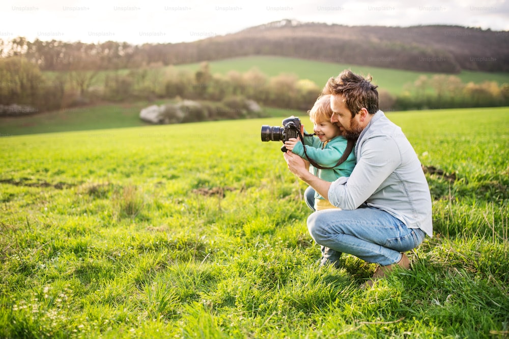 Ein Vater und sein kleiner Sohn mit einer Kamera draußen in der grünen, sonnigen Frühlingsnatur.