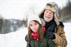 Nonno anziano e una bambina che si divertono sulla neve in una giornata invernale.