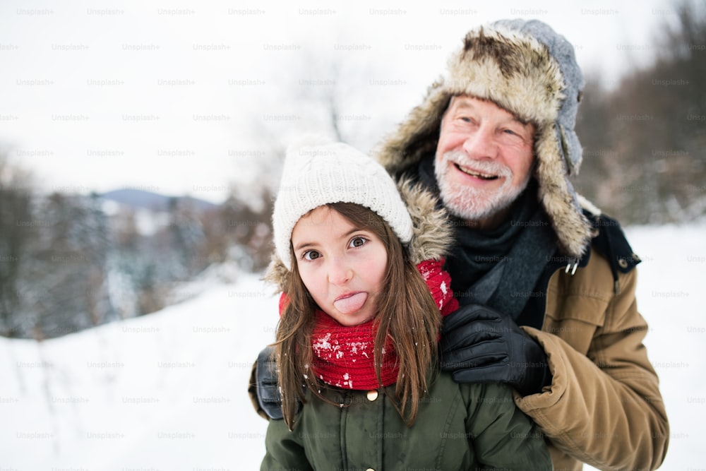 Avô sênior e uma menina pequena se divertindo na neve em um dia de inverno.