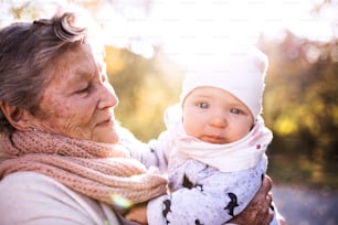 An elderly woman with a baby in autumn nature. Senior woman on a walk.