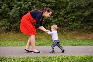 Cute little boy making first steps in nature. Young mother with her toddler boy in nature. Summer time.