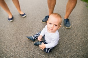 Little boy with unrecognizable parents sitting on the pavement in nature. Summer time.