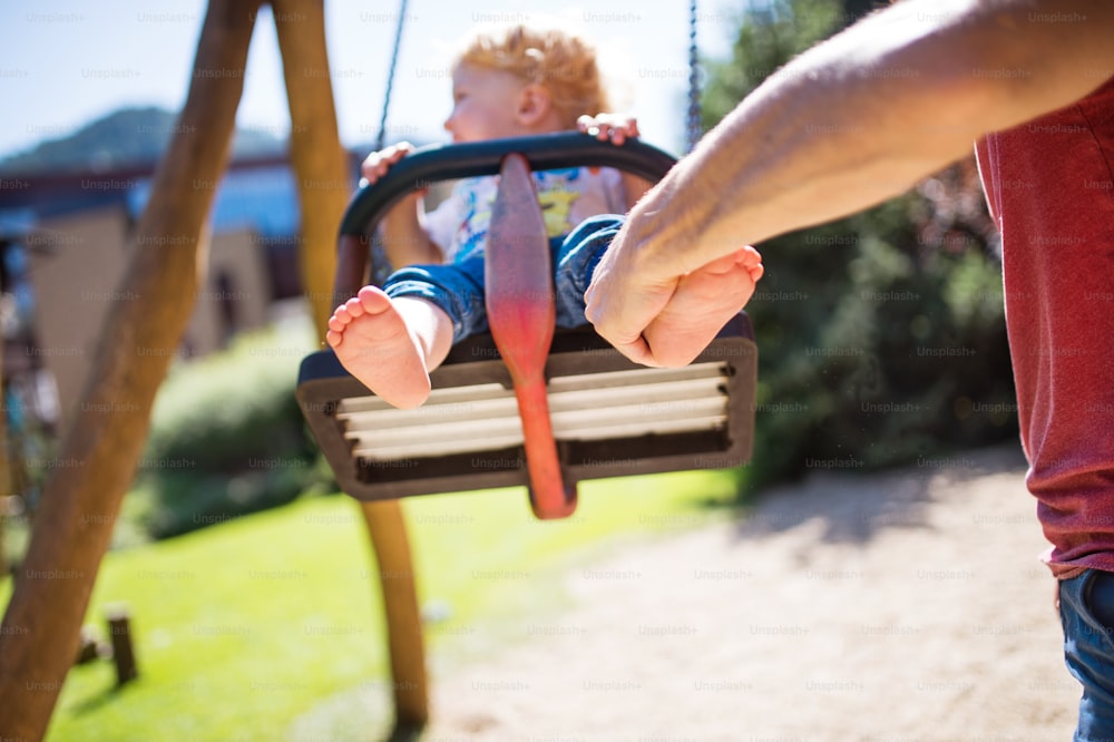 Cute little boy with unrecognizable father on the swing at the playground.