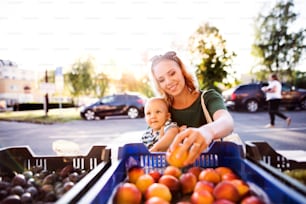 Madre joven con su bebé comprando en el mercado al aire libre.