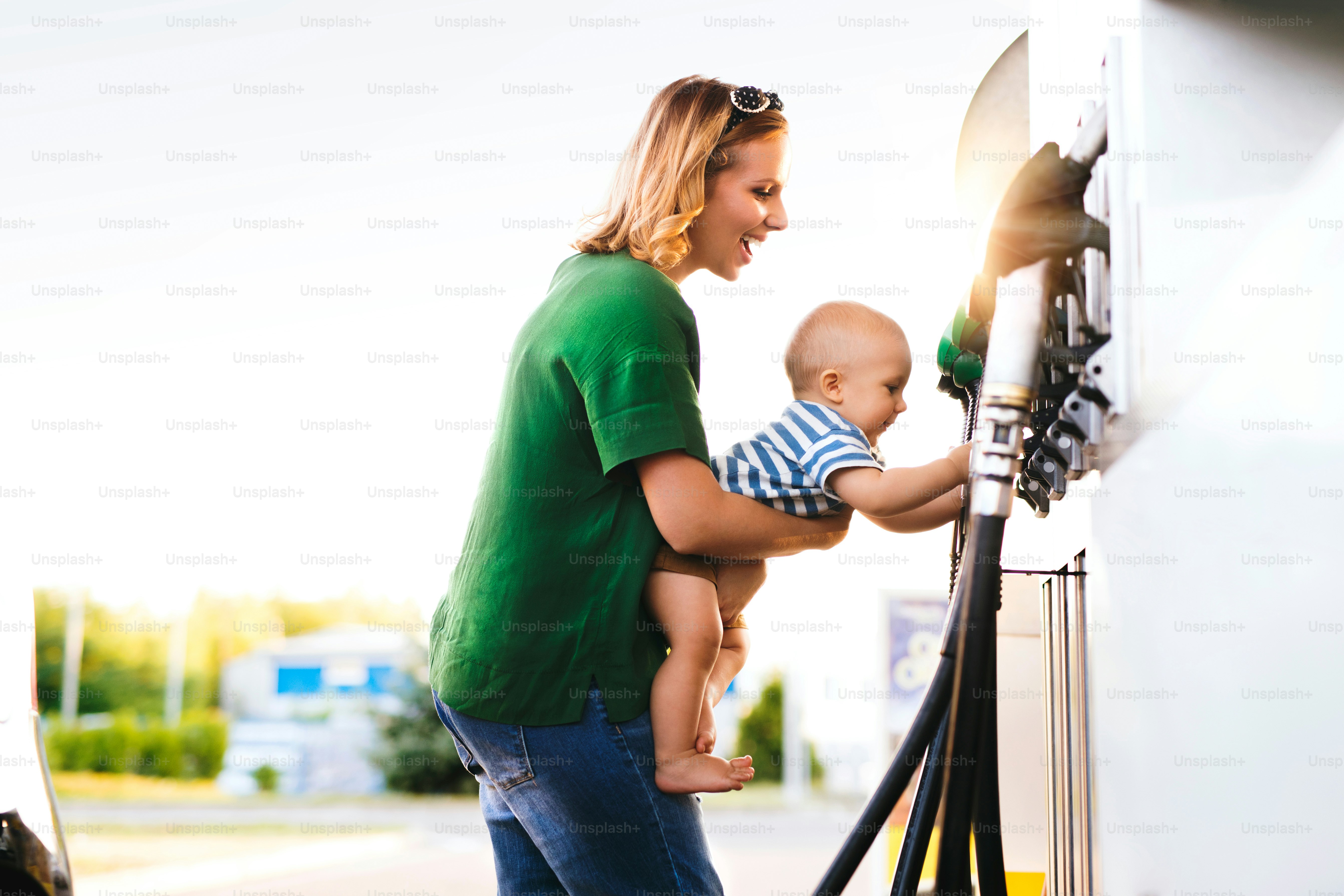 Young mother with baby boy at the petrol station going to refuel the