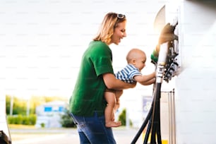 Madre joven con un bebé varón en la gasolinera va a repostar el coche.