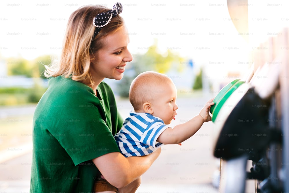 주유소에서 아기를 안고 있는 젊은 엄마가 차에 연료를 보급하러 간다.