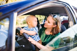 Junge Mutter mit ihrem kleinen Sohn im Auto. Eine Frau und ein kleiner Junge, die so tun, als würden sie fahren.