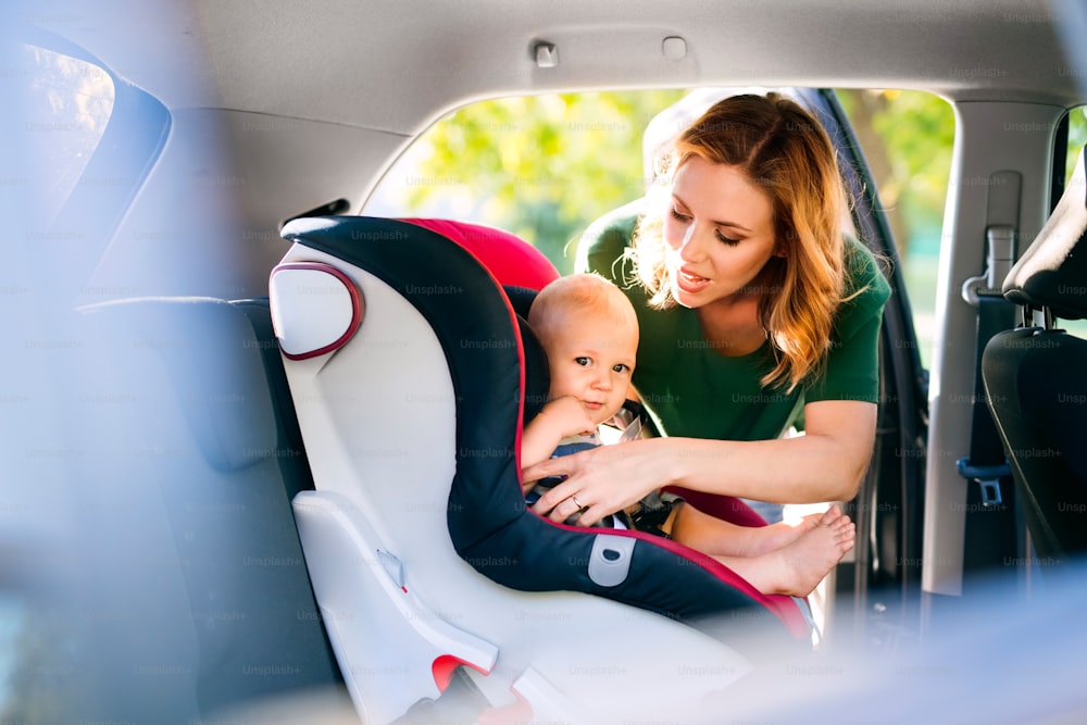 Giovane madre che mette il suo bambino nel seggiolino dell'auto, allacciando le cinture di sicurezza.