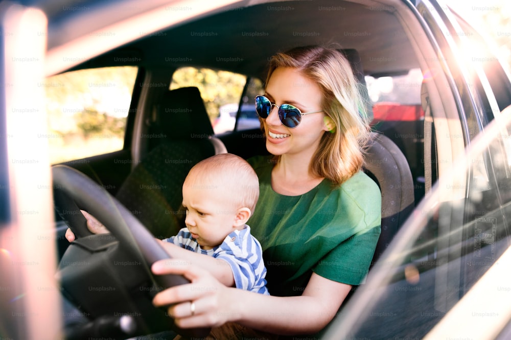 차에 어린 아들을 안고 있는 젊은 엄마. 운전하는 척하는 여자와 남자 아기.