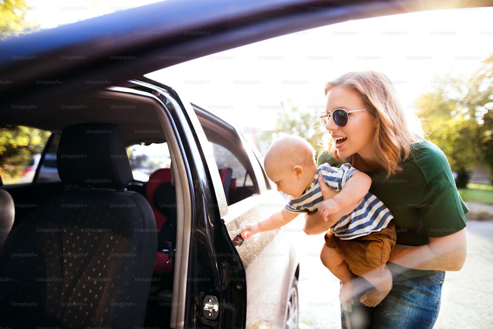 La joven madre sostiene a su pequeño bebé en los brazos al subir al auto. Disparado a través del vidrio.