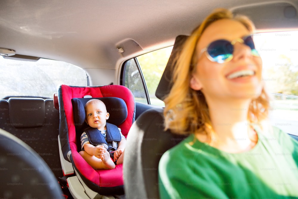 Jovem mãe com seu filho pequeno no carro. Uma mulher dirigindo e um menino sentado em um assento de carro.