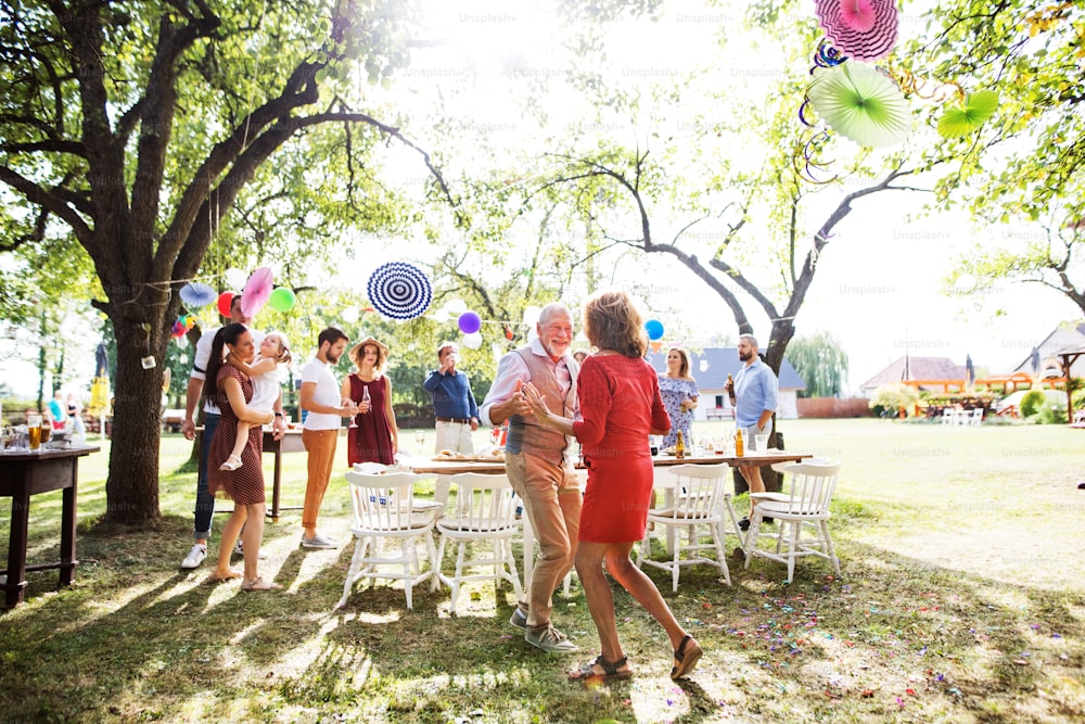 Una pareja de ancianos bailando en una fiesta en el jardín o una celebración familiar afuera en el patio trasero.