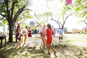 A senior couple dancing on a garden party or family celebration outside in the backyard.