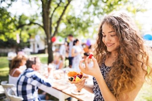 Family celebration outside in the backyard. Big garden party. A teenage girl eating fruit.