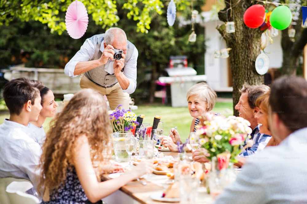 Family celebration outside in the backyard. Big garden party. Grandfather taking photo with a camera.