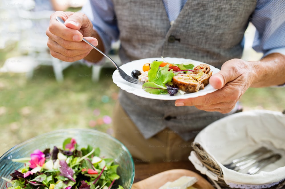 Unrecognizable man with a plate with food. Family celebration outside in the backyard. Big garden party.