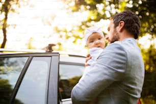 El joven padre sostiene a su pequeña niña en los brazos que entran en el auto.