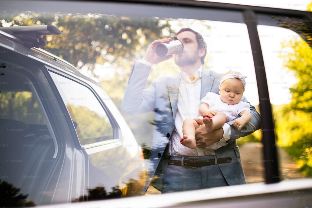 Giovane padre che trasporta la sua bambina. Uomo alla macchina, bevendo caffè. Girato attraverso il vetro.