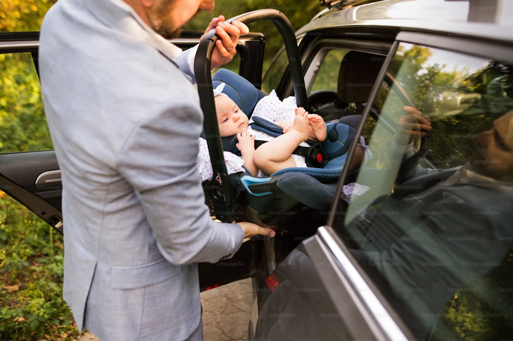 알아볼 수 없는 남자가 차에 여자 아기와 함께 카시트를 놓고 있다.