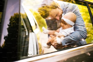 Giovane padre che tiene la sua bambina tra le braccia andando in macchina. Girato attraverso il vetro.