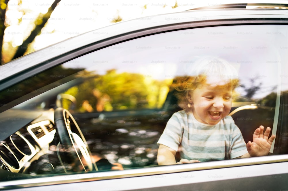 Cute little boy playing in the car, looking out of window, waving.