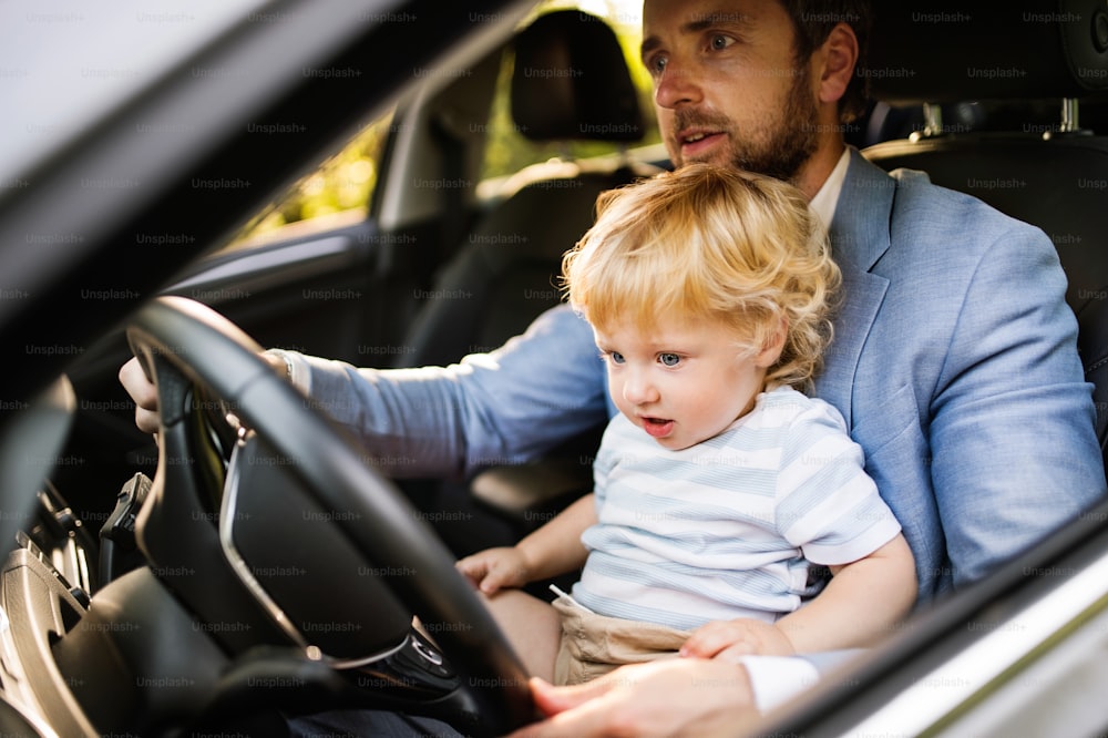 Man driving a car with little son. Toddler boy sitting in his fathers lap.