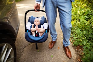 Unrecognizable man carrying his baby girl in a car seat. Man with a baby by the car.