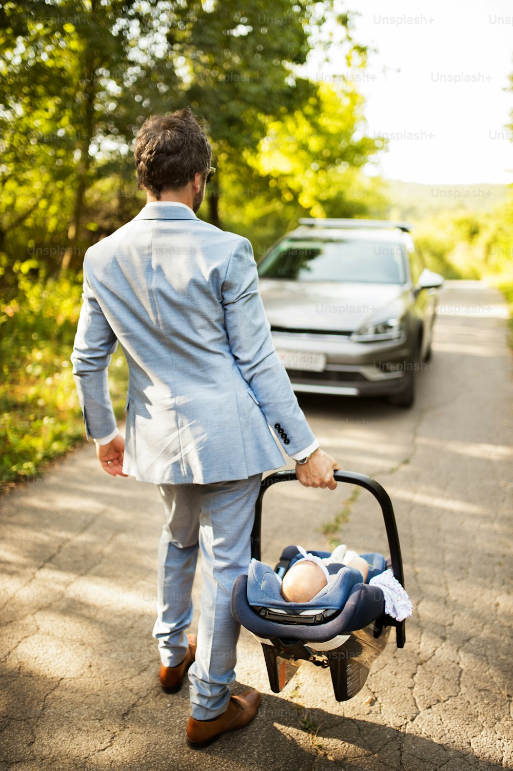 Pai jovem carregando seu pequeno bebê em uma cadeirinha, entrando no carro.