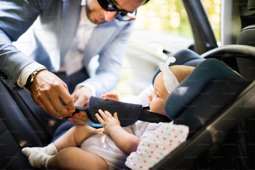 女の赤ちゃんを車に乗せている認識できない男。シートベルトを締める父。