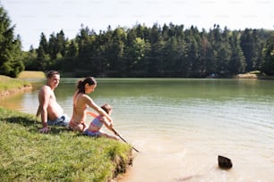 Giovane madre e padre con la loro figlia al lago. Caldo estivo e acqua.