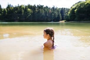 Nettes kleines Mädchen im Badeanzug, das am See steht. Sommerhitze und Wasser.
