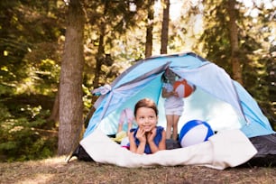 Two beautiful little girls with colorful beach balls sitting in tent, camping by the lake.