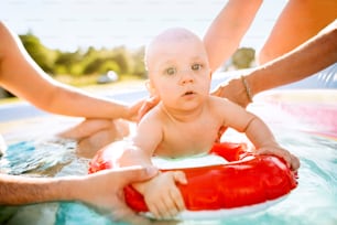 Pequeño bebé con sus padres irreconocibles en la piscina del jardín. Horario de verano.