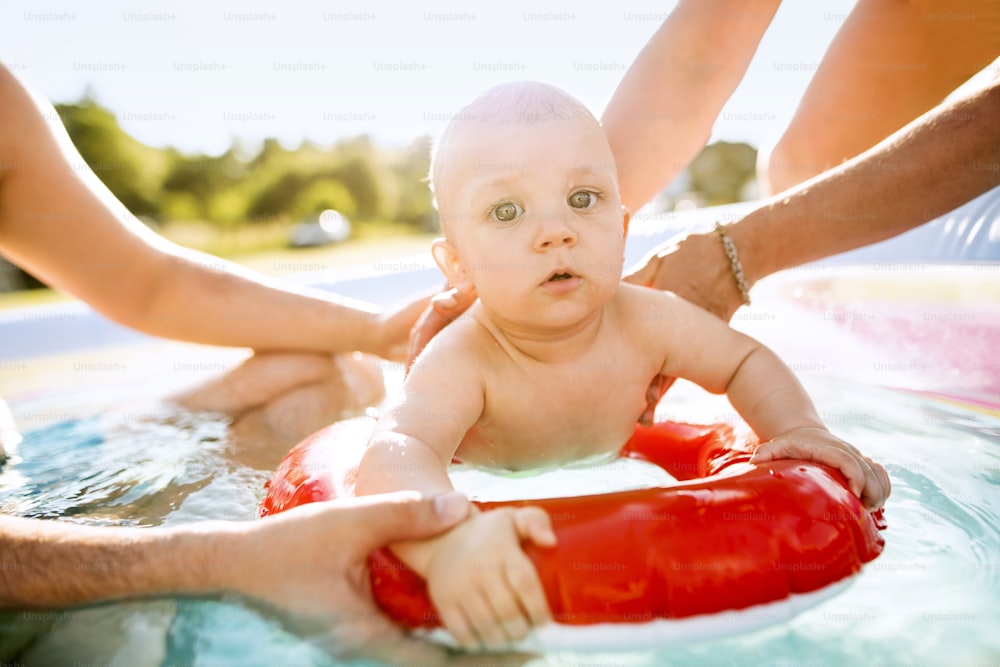 Little baby boy with his unrecognizable parents in the swimming pool in the garden. Summer time.
