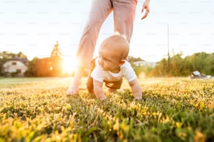 Lindo bebé con su madre irreconocible arrastrándose afuera sobre la hierba verde.