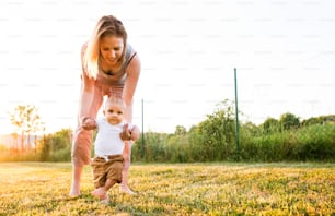 Beautiful young mother with her baby son. First steps.