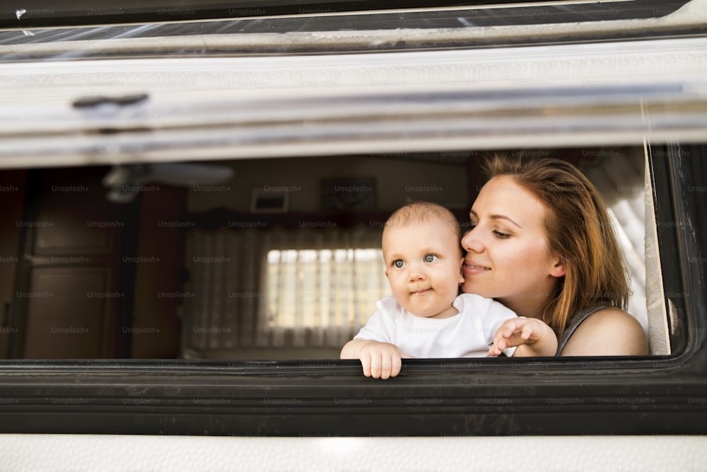 Beautiful young mother and her baby son in a camper van on a summer day.